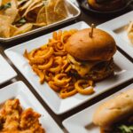 Restaurant table with square white plates full of yummy food; burgers and fries, chicken and waffles