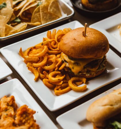 Restaurant table with square white plates full of yummy food; burgers and fries, chicken and waffles